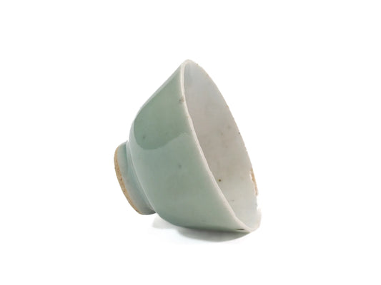 Tilted side view of an antique Mid-Qing Dynasty Celadon cup showing the pale green celadon glaze, white interior and small rim wear