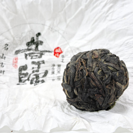 Close-up of unwrapped Xi Gui (昔归) Ancient Tree Raw Pu’er Tea ball showing dry leaf texture on traditional wrapper