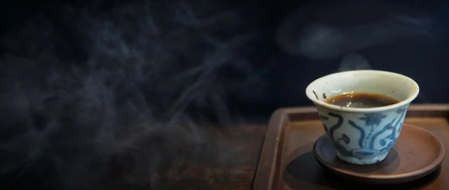 A steaming cup of premium aged Puerh tea in a vintage blue and white porcelain cup, set against a dark moody background to celebrate Cha Zhi Ji's 30 years of tea heritage.