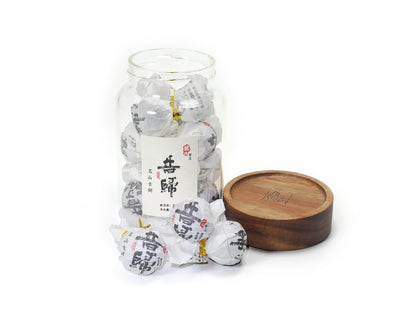 Opened jar of Xi Gui (昔归) Ancient Tree Raw Pu’er Tea with wooden lid beside it – individually wrapped tea balls displayed