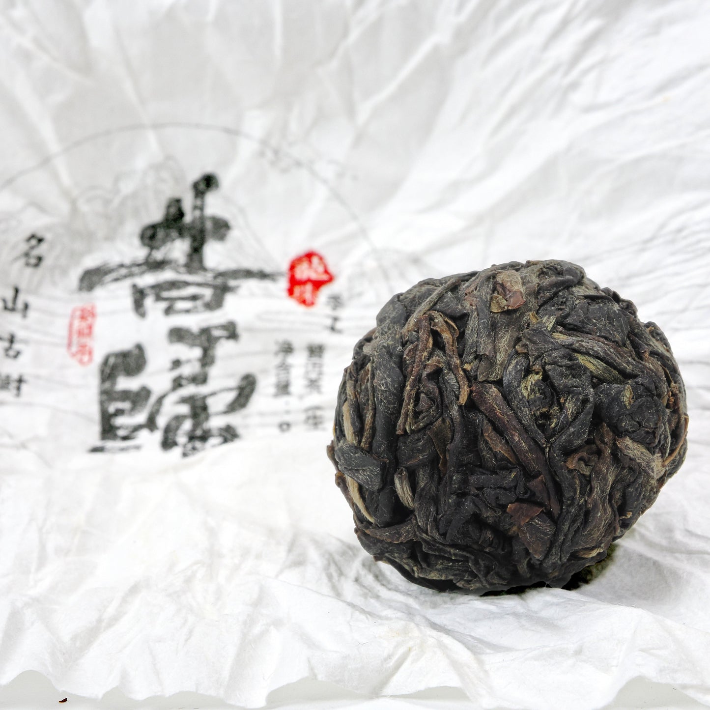 Close-up of unwrapped Xi Gui (昔归) Ancient Tree Raw Pu’er Tea ball showing dry leaf texture on traditional wrapper