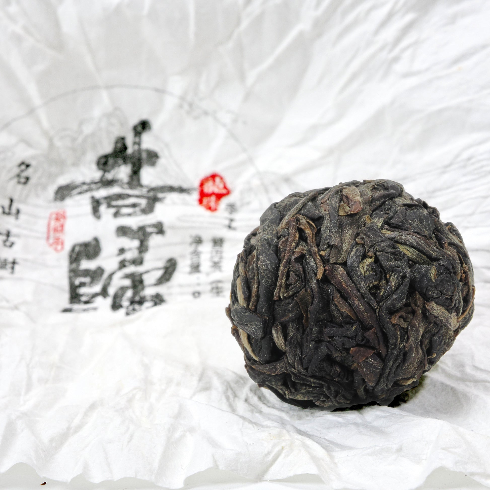 Close-up of unwrapped Xi Gui (昔归) Ancient Tree Raw Pu’er Tea ball showing dry leaf texture on traditional wrapper