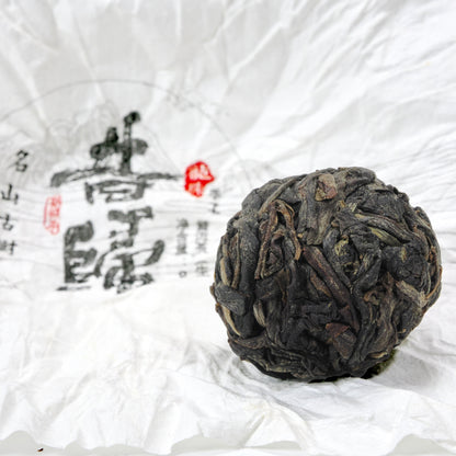 Close-up of unwrapped Xi Gui (昔归) Ancient Tree Raw Pu’er Tea ball showing dry leaf texture on traditional wrapper